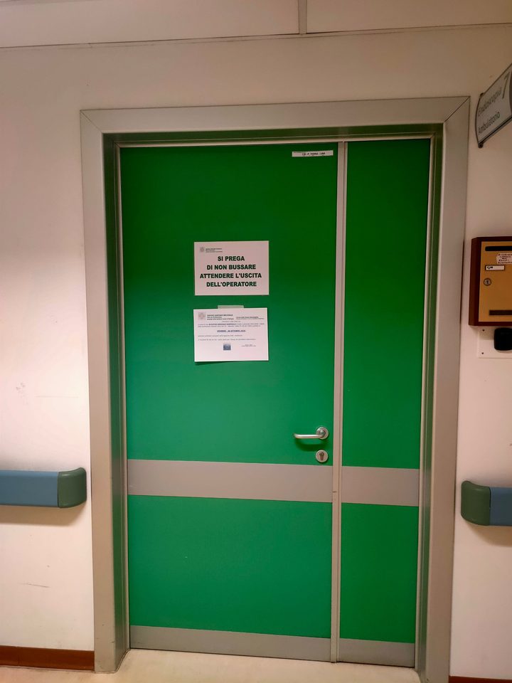 Porta verde di un ambulatorio d'ospedale con il cartello «Si prega di non bussare, attendere l'uscita dell'operatore»