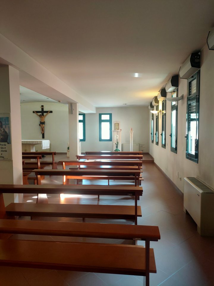 La navata laterale della cappella con cinque finestre sulla parete destra, il tabernacolo in fondo e il crocifisso a sinistra